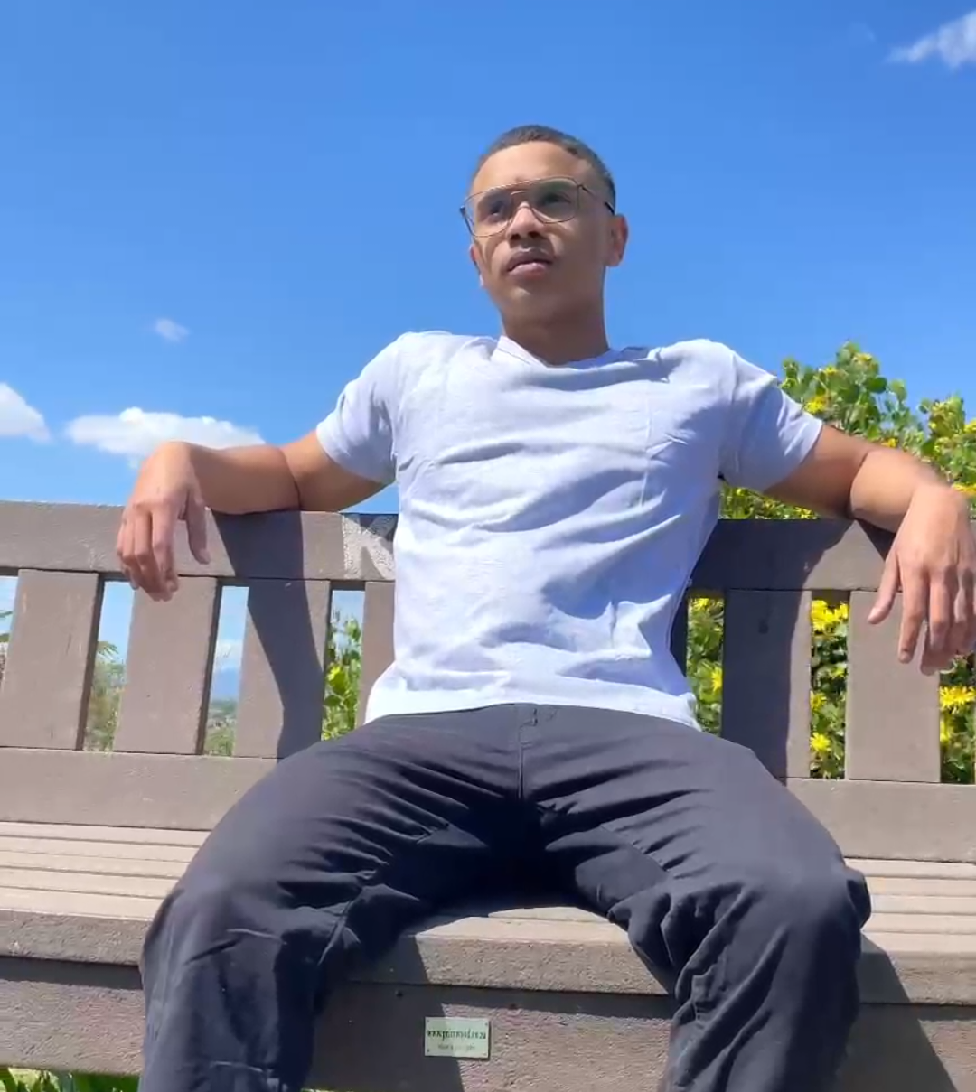 V-neck cotton t-shirt in white, worn by a person sitting on a bench outdoors.